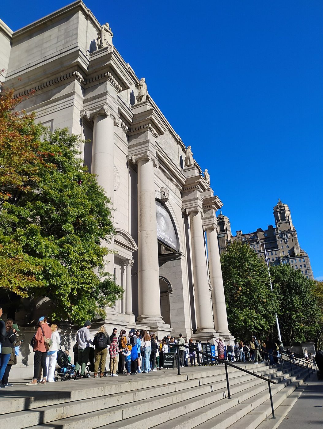 Visitors lining up on the steps of the museum's Central Park West facade under a blue sky