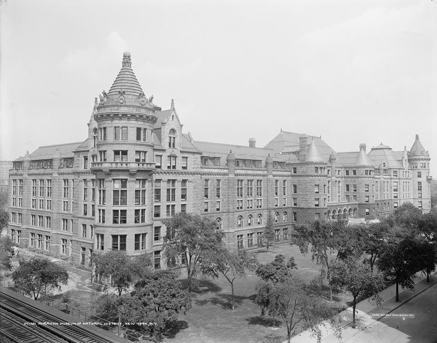 An early photograph of the Romanesque Revival museum building with turrets and a roofline of dormers, seen across a park