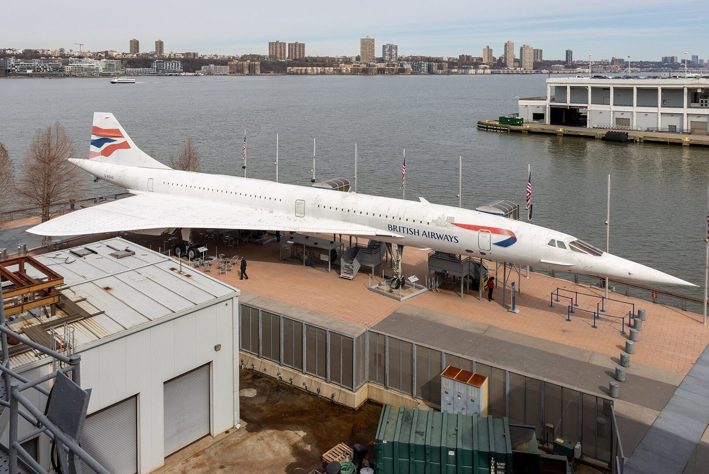 A white British Airways Concorde on a pier beside the Hudson River with the New Jersey shoreline behind it
