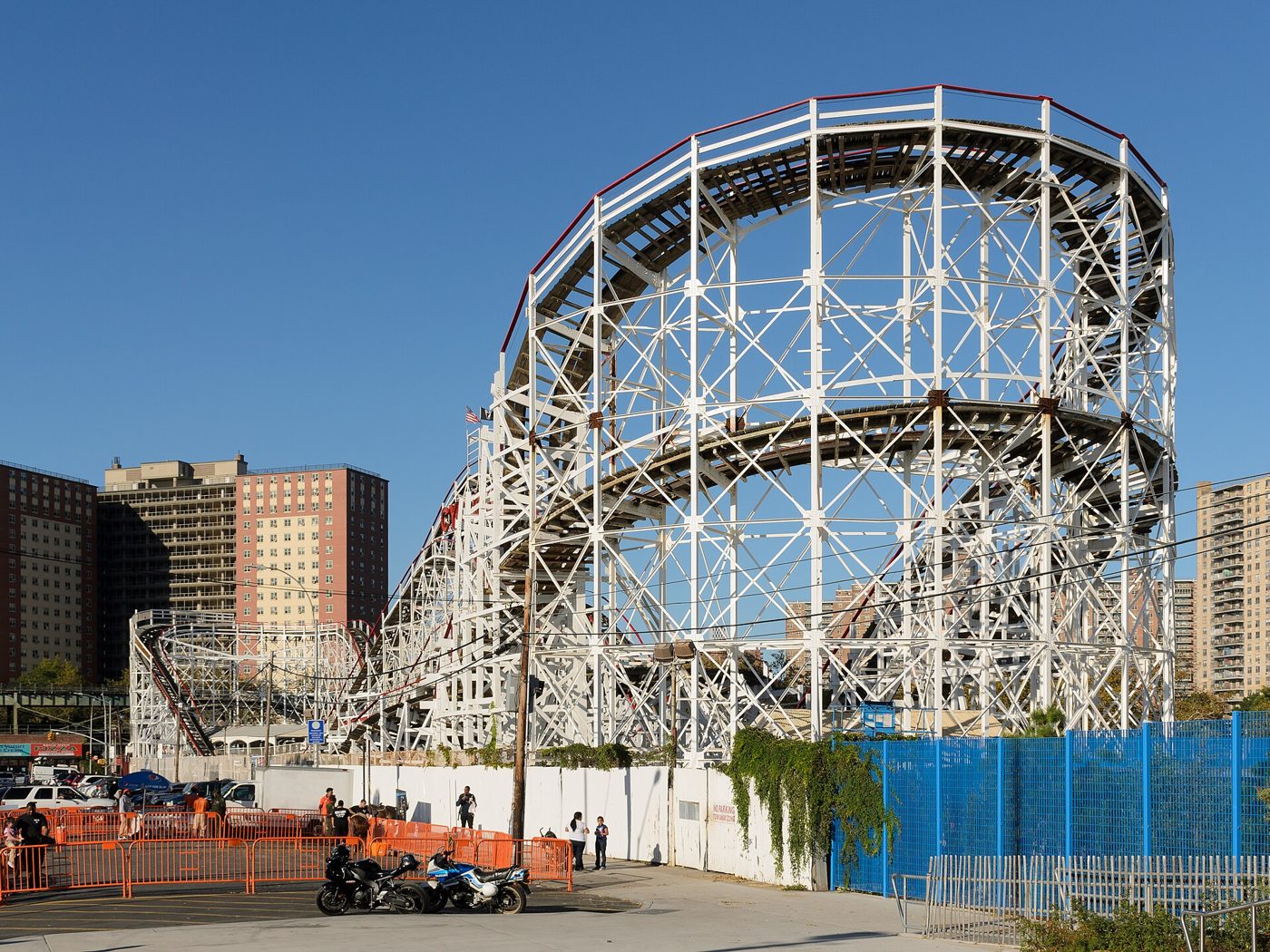 The white wooden frame of the Cyclone roller coaster rising behind a fence beside a city street in Coney Island