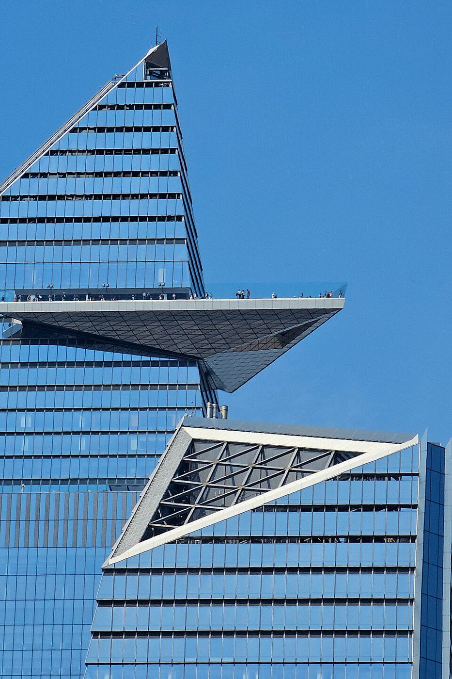 Visitors on the Edge observation deck with tilted glass walls, seen from the deck, with buildings of Midtown beyond