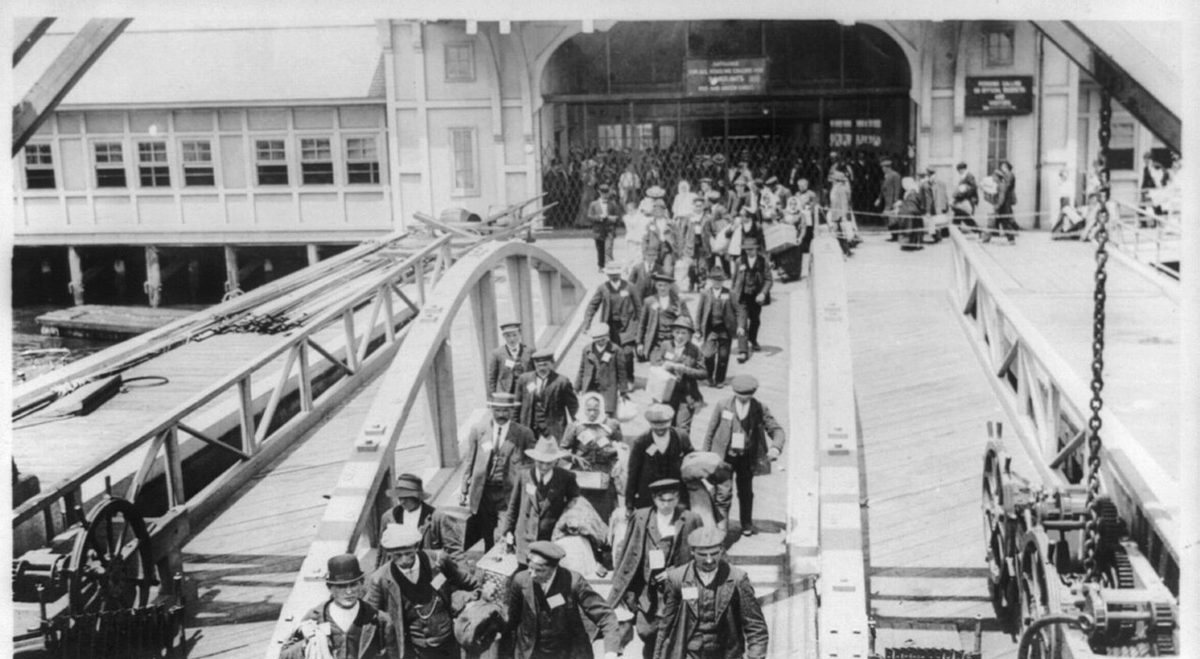Immigrants walking along a gangway toward the Ellis Island immigration building