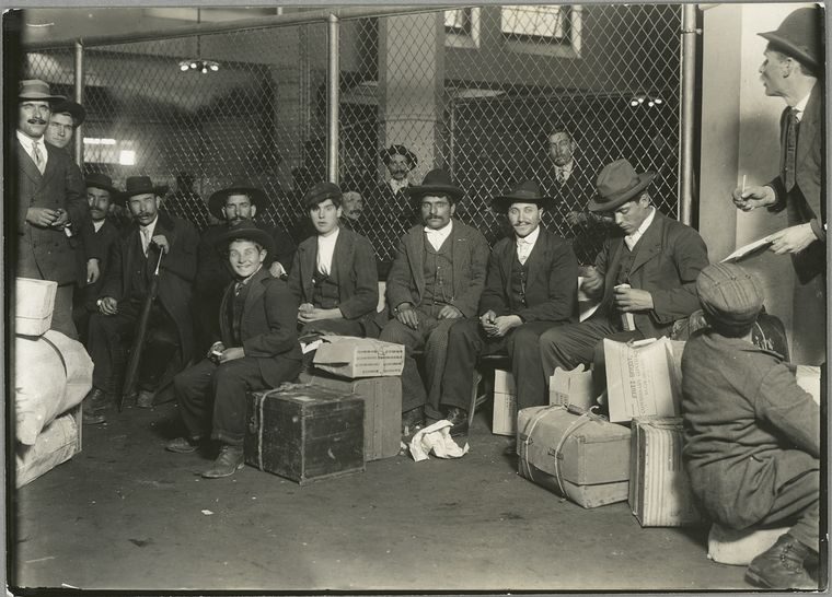Italian immigrants sitting with their luggage while waiting at Ellis Island