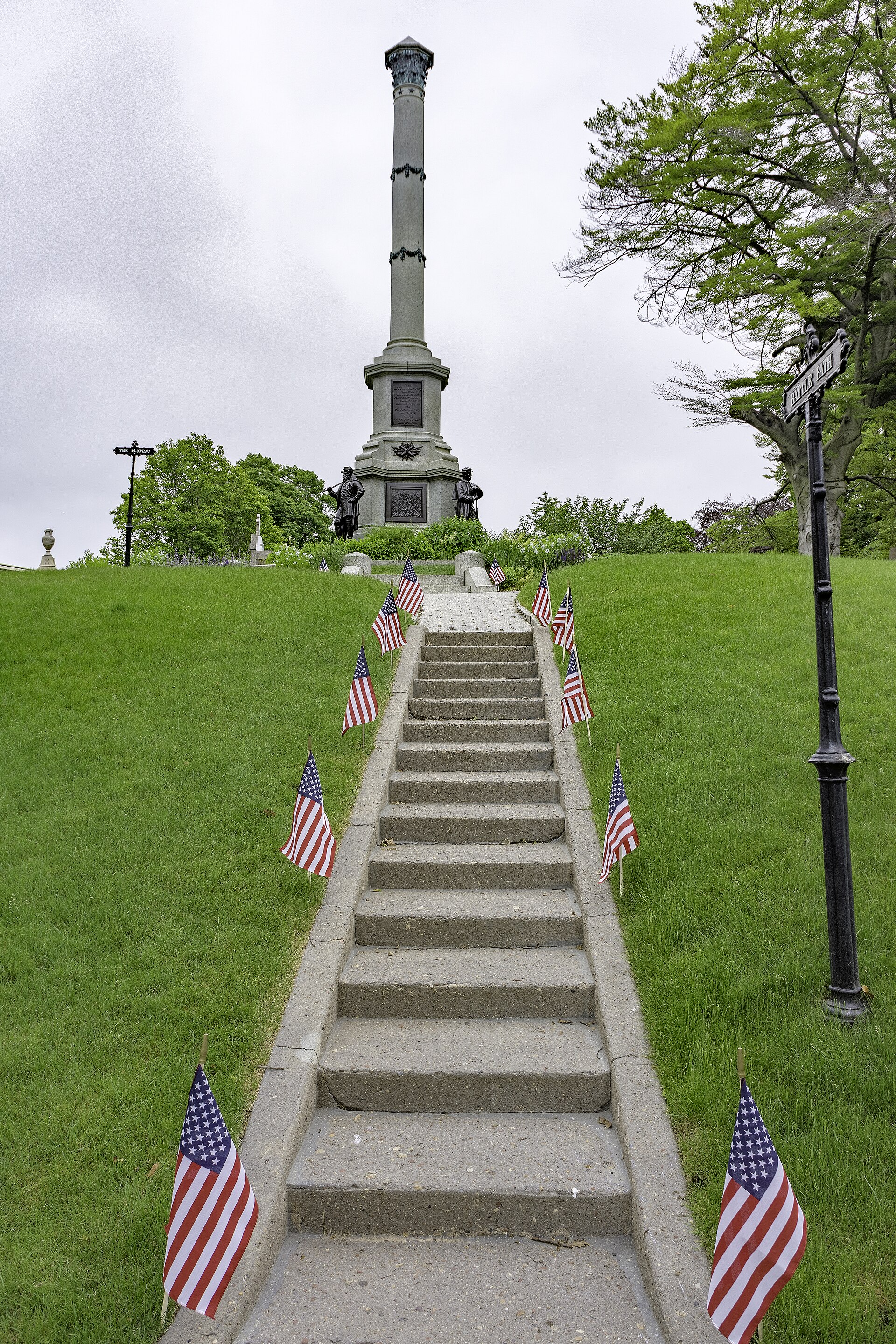 Stone steps leading up Battle Hill, lined with small American flags, toward a tall monument column