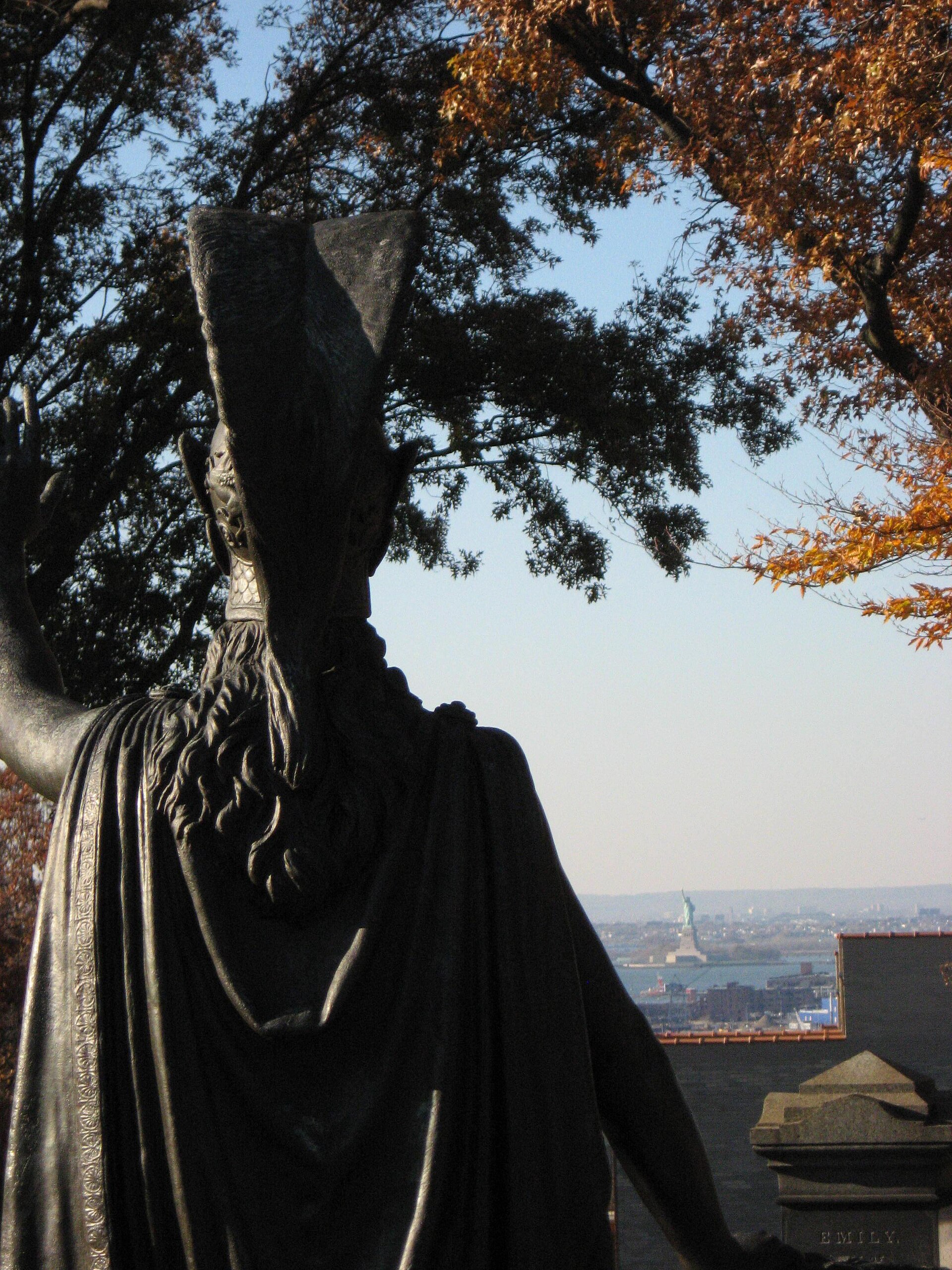 The bronze Minerva statue silhouetted against the sky, with the Statue of Liberty visible in the harbor beyond