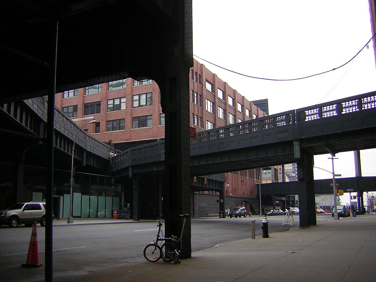 View along Tenth Avenue from beneath the High Line, with steel columns, a brick building and a rail siding entering the wall of a building