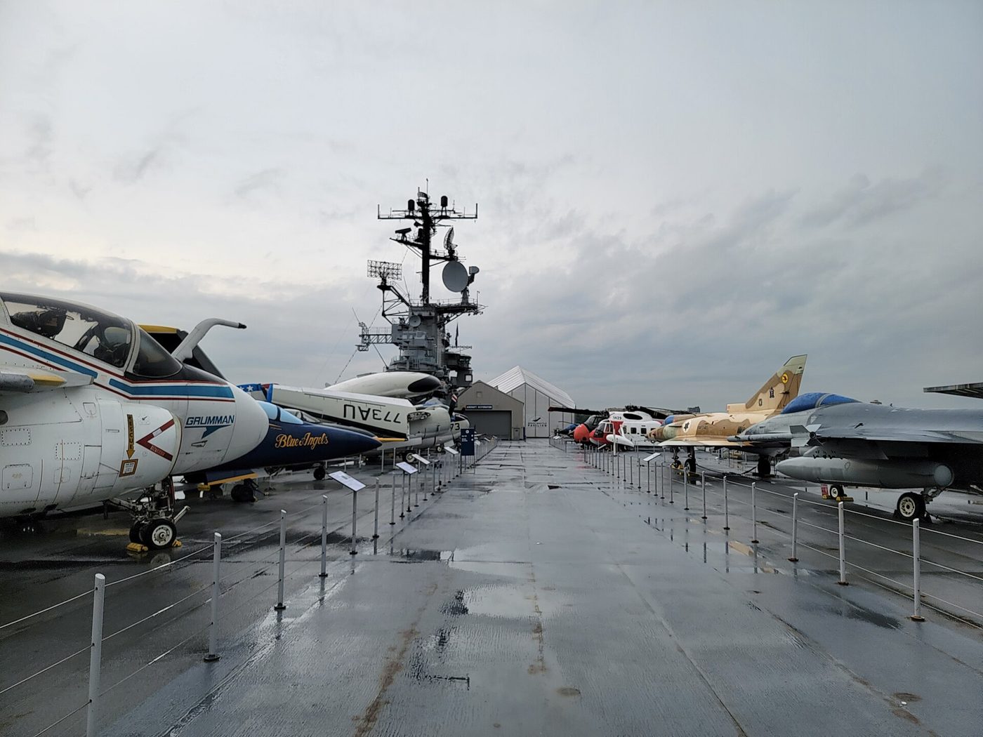 Aircraft parked on the flight deck of the Intrepid under a grey sky, with the carrier island and radar mast behind them