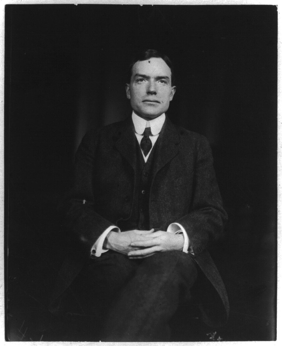 John D. Rockefeller Jr. seated in a dark suit with his hands clasped