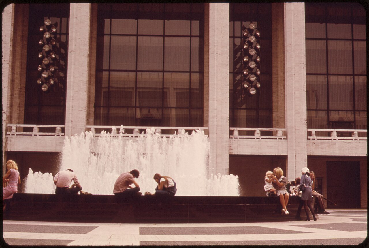 People sitting on the edge of the Revson Fountain at Lincoln Center in 1973, with water spraying behind them