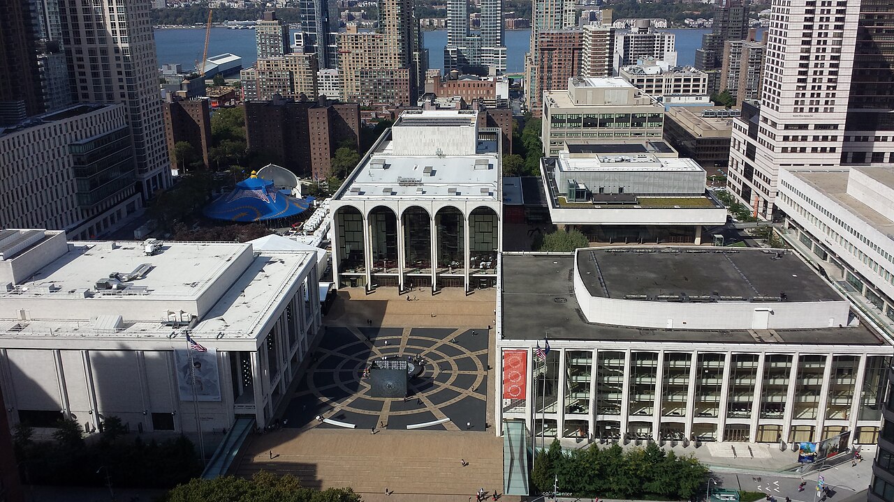 An aerial view of the Lincoln Center plaza with the arches of the Metropolitan Opera House at the far end and a circular pattern in the paving