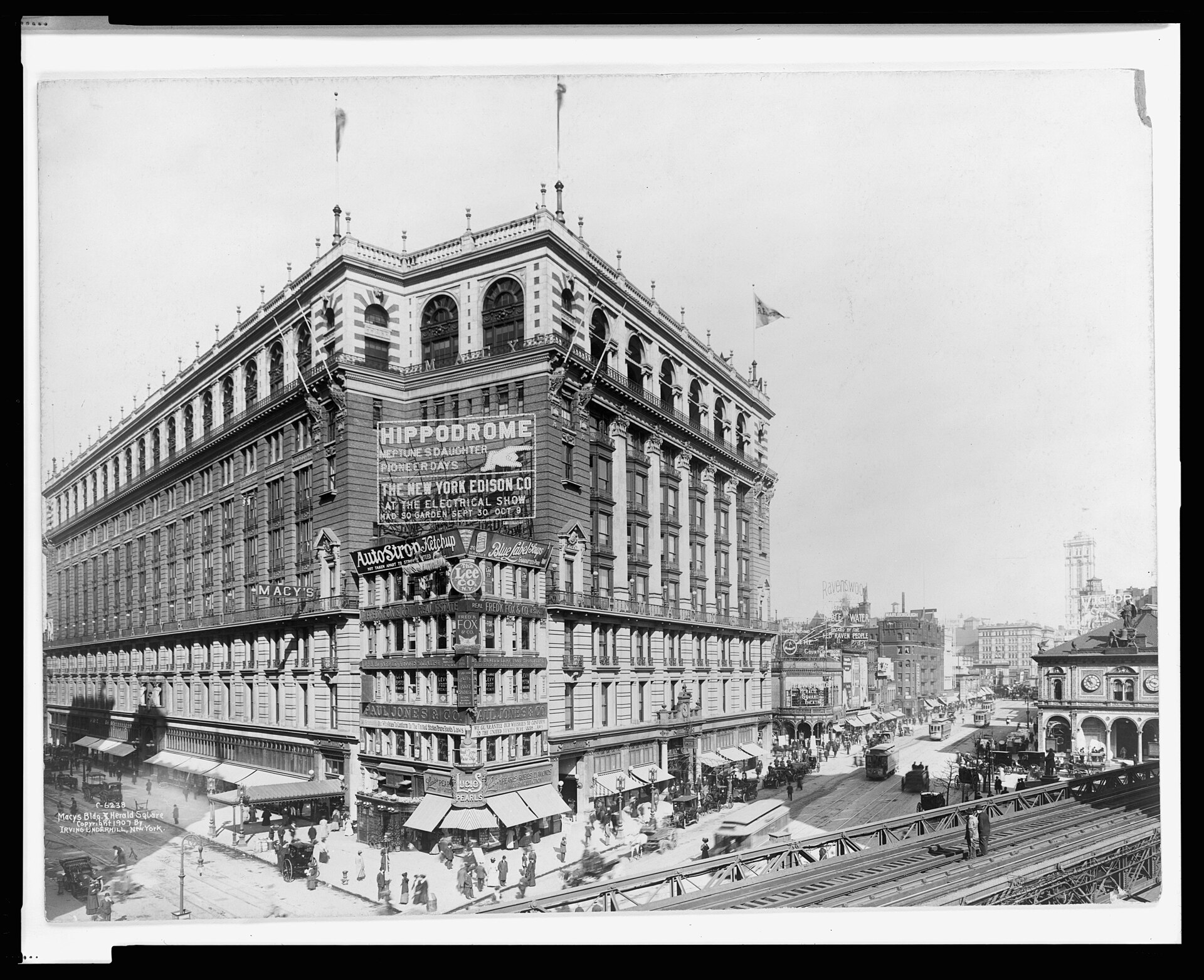 Macy's department store and Herald Square in 1907, a nine-story white building with a corner tower, elevated train tracks and streetcars in the foreground