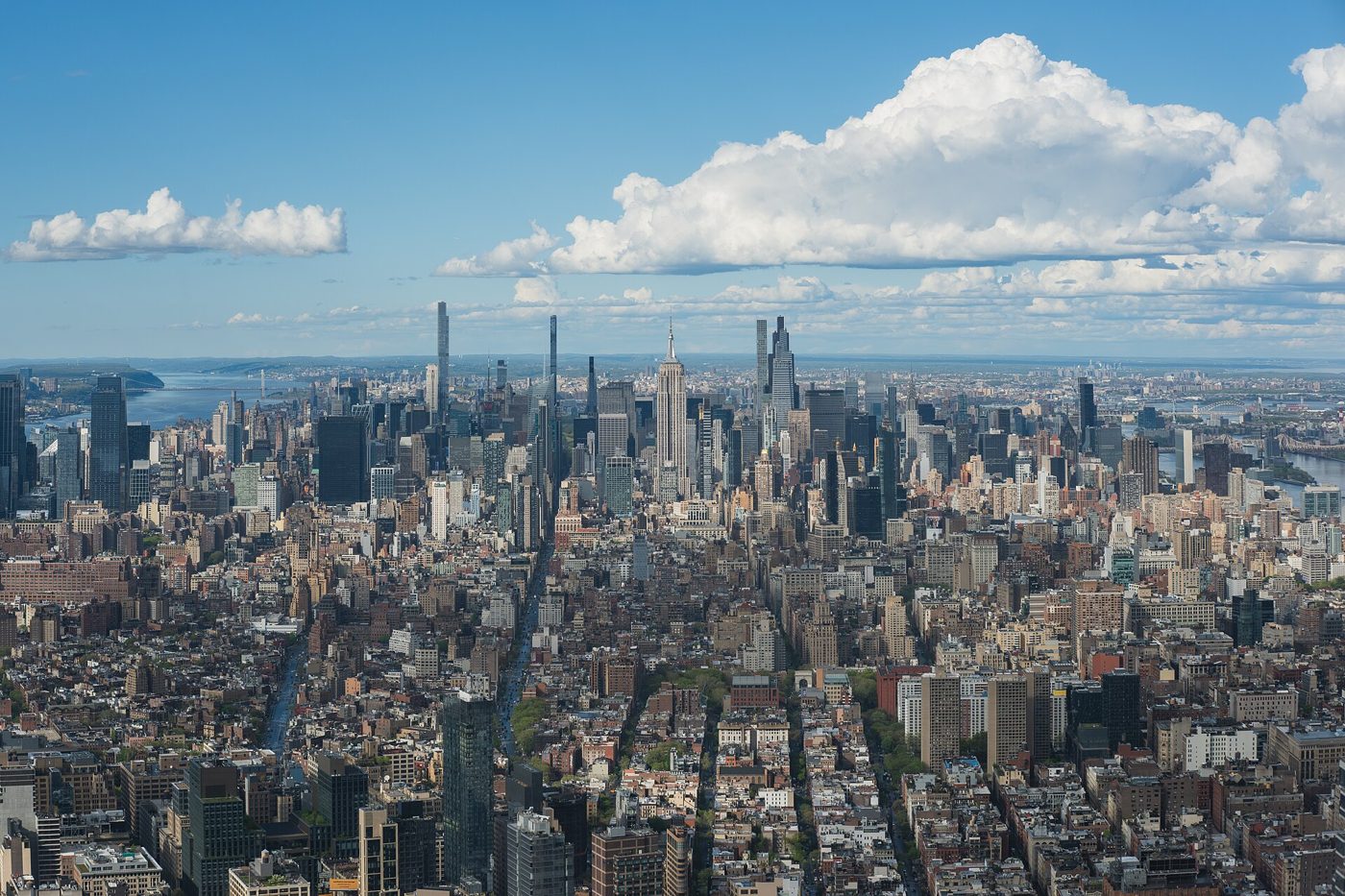 Aerial panorama of Midtown Manhattan under a blue sky with large clouds, seen from a high floor