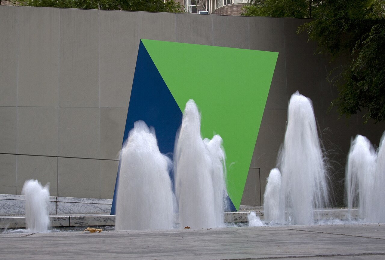 The courtyard at MoMA with water jets rising in front of a large painted wall in blue and green