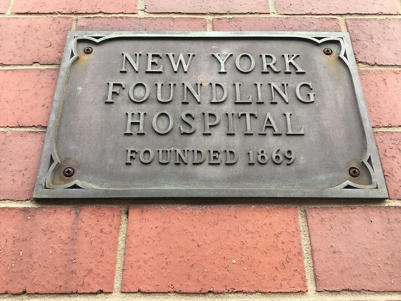 Bronze plaque reading New York Foundling Hospital Founded 1869 set into red brick at East 69th Street, Manhattan