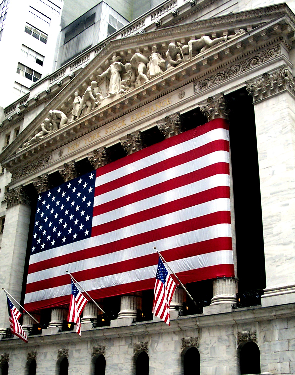 The New York Stock Exchange facade, its six tall columns and sculpture-filled pediment partly covered by a huge American flag