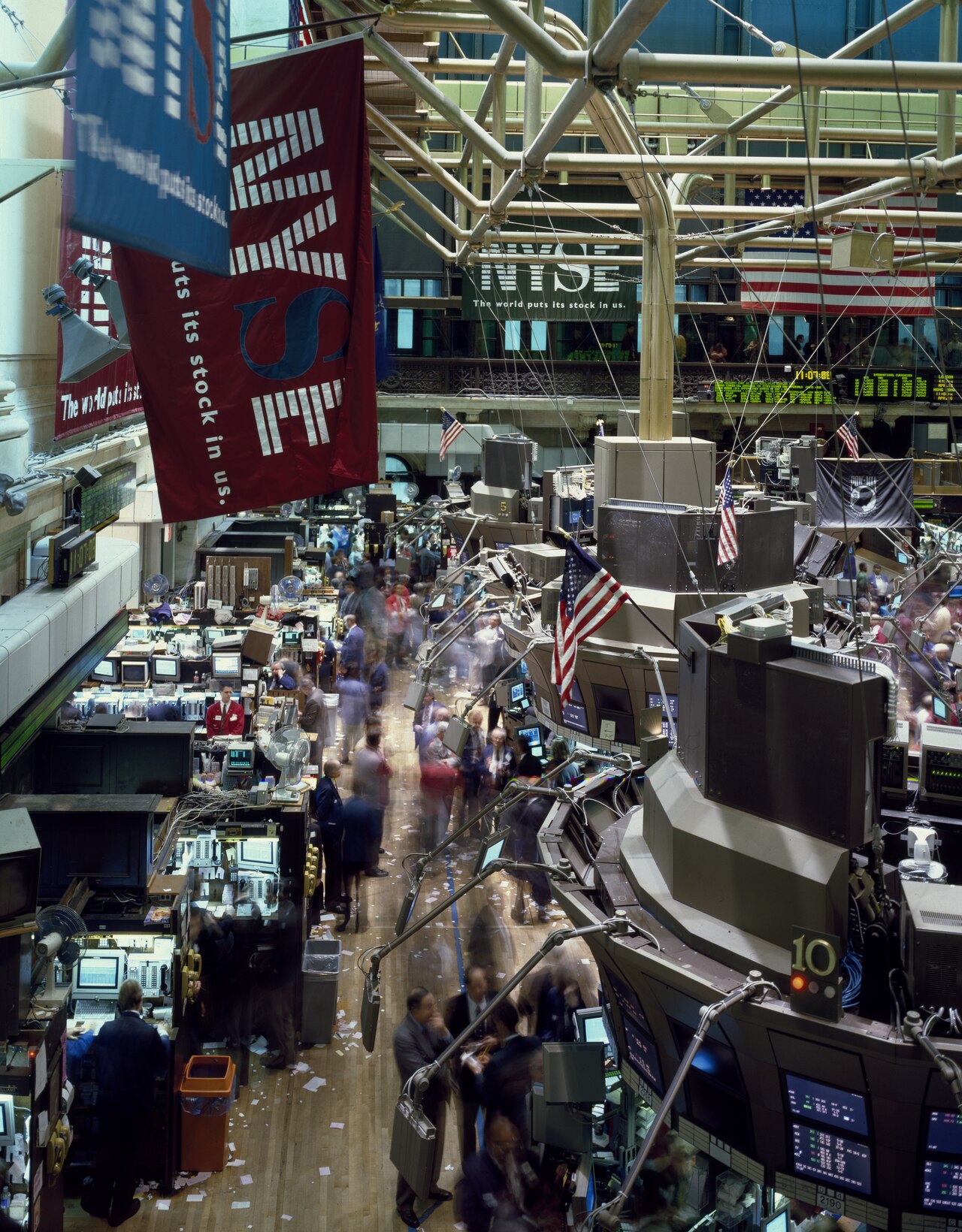 The modern NYSE trading floor seen from above, trading posts with screens under a large American flag