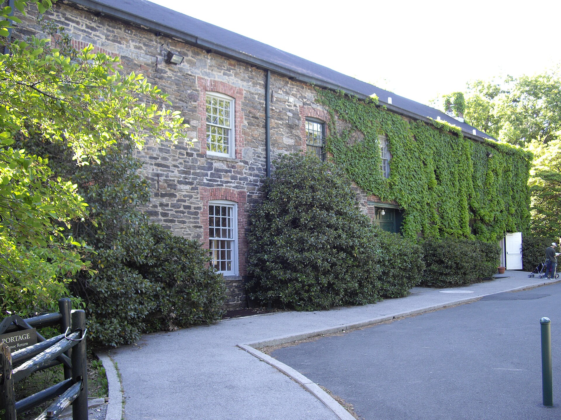 A long stone industrial building, the Lorillard Snuff Mill, partly covered in ivy, beside a road