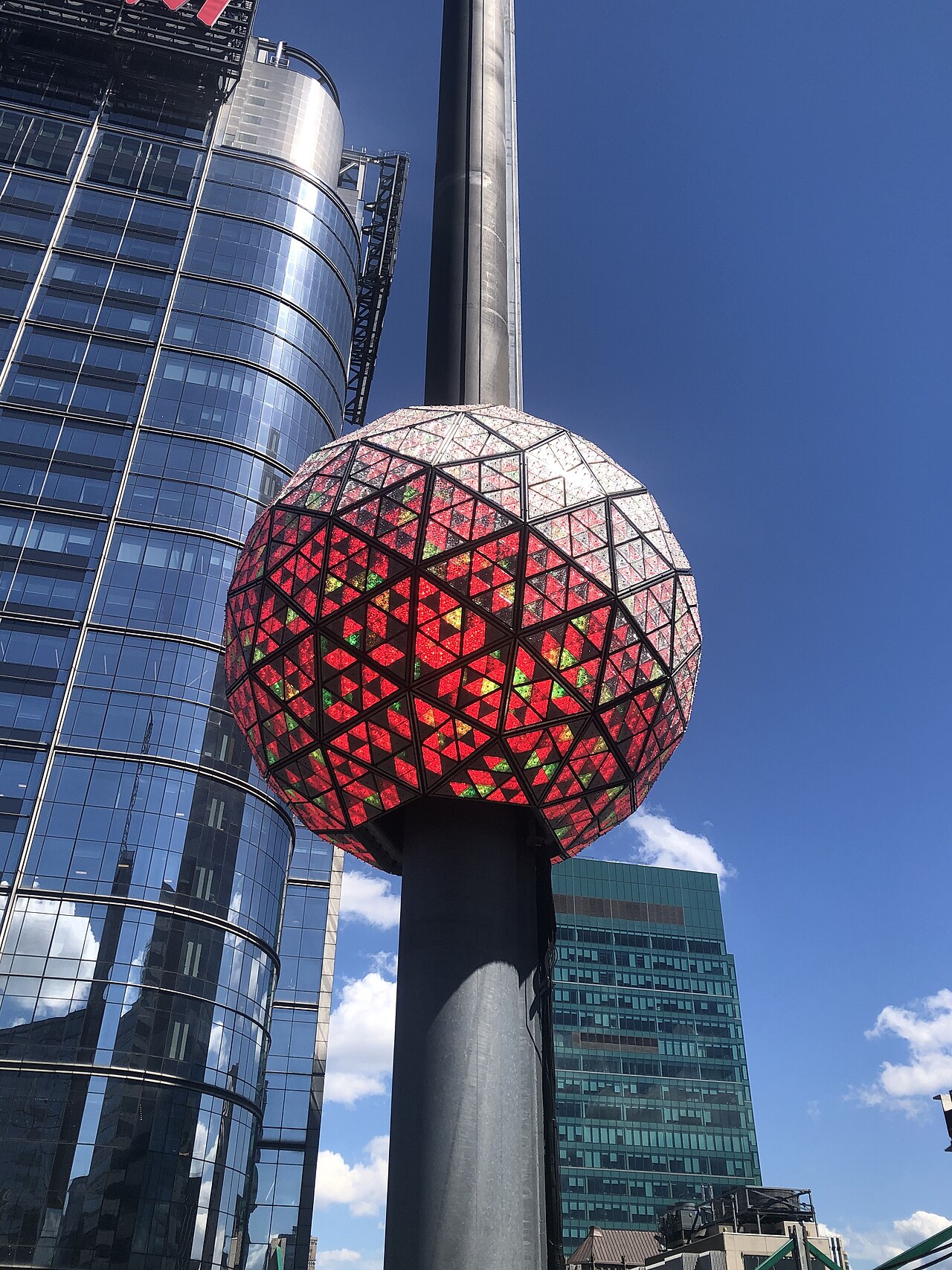 The New Year's Eve Ball, a sphere of triangular crystal panels glowing red, mounted on its pole against surrounding towers