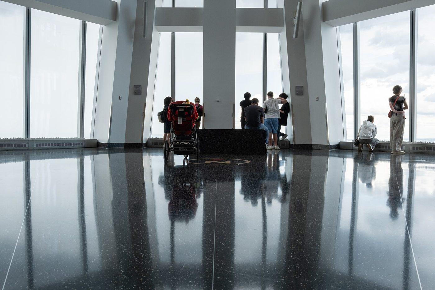 The interior of One World Observatory with visitors standing in silhouette against tall floor-to-ceiling windows