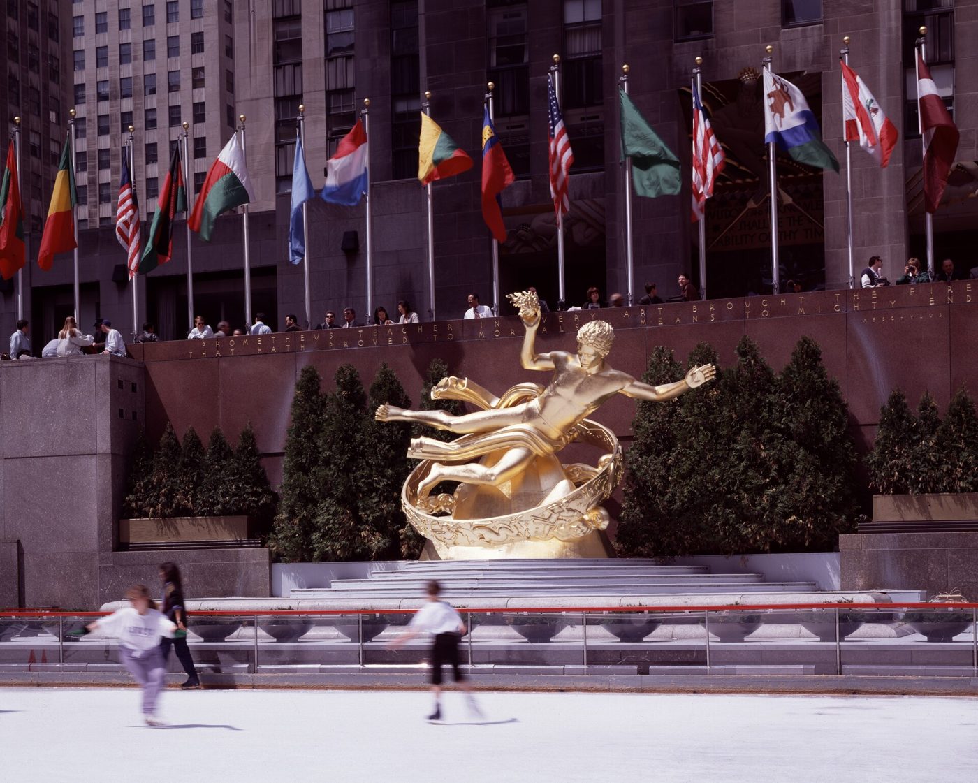 The gilded Prometheus statue above the sunken plaza and skating rink at Rockefeller Center with flags behind