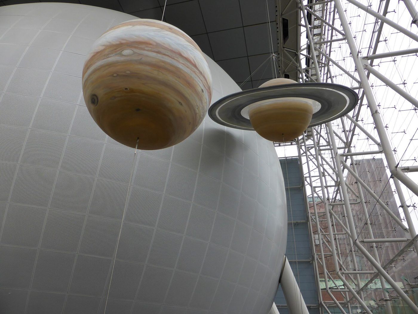 The white Hayden Sphere with models of Jupiter and Saturn hanging in front of it inside the Rose Center
