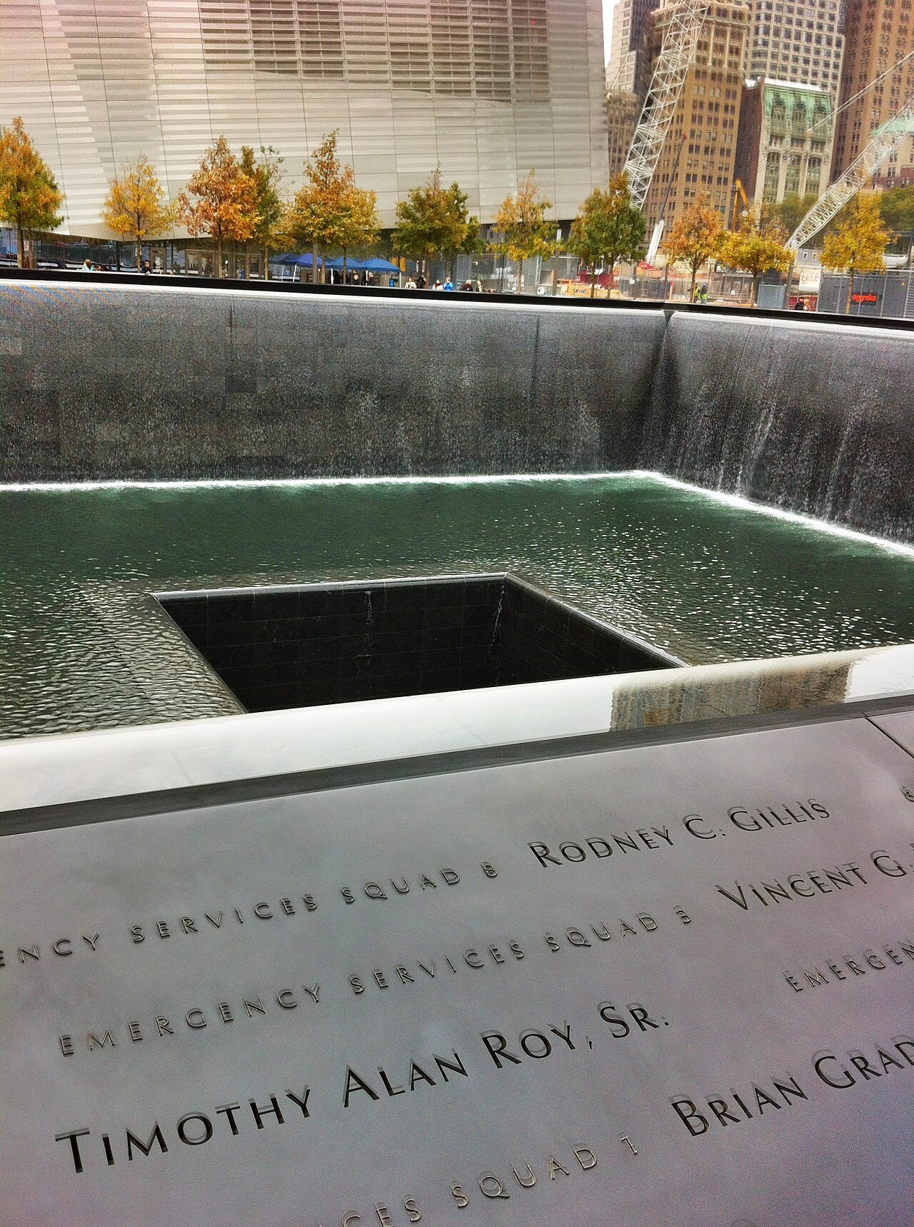 The corner of a reflecting pool with waterfalls and, in the foreground, a bronze parapet incised with victims' names