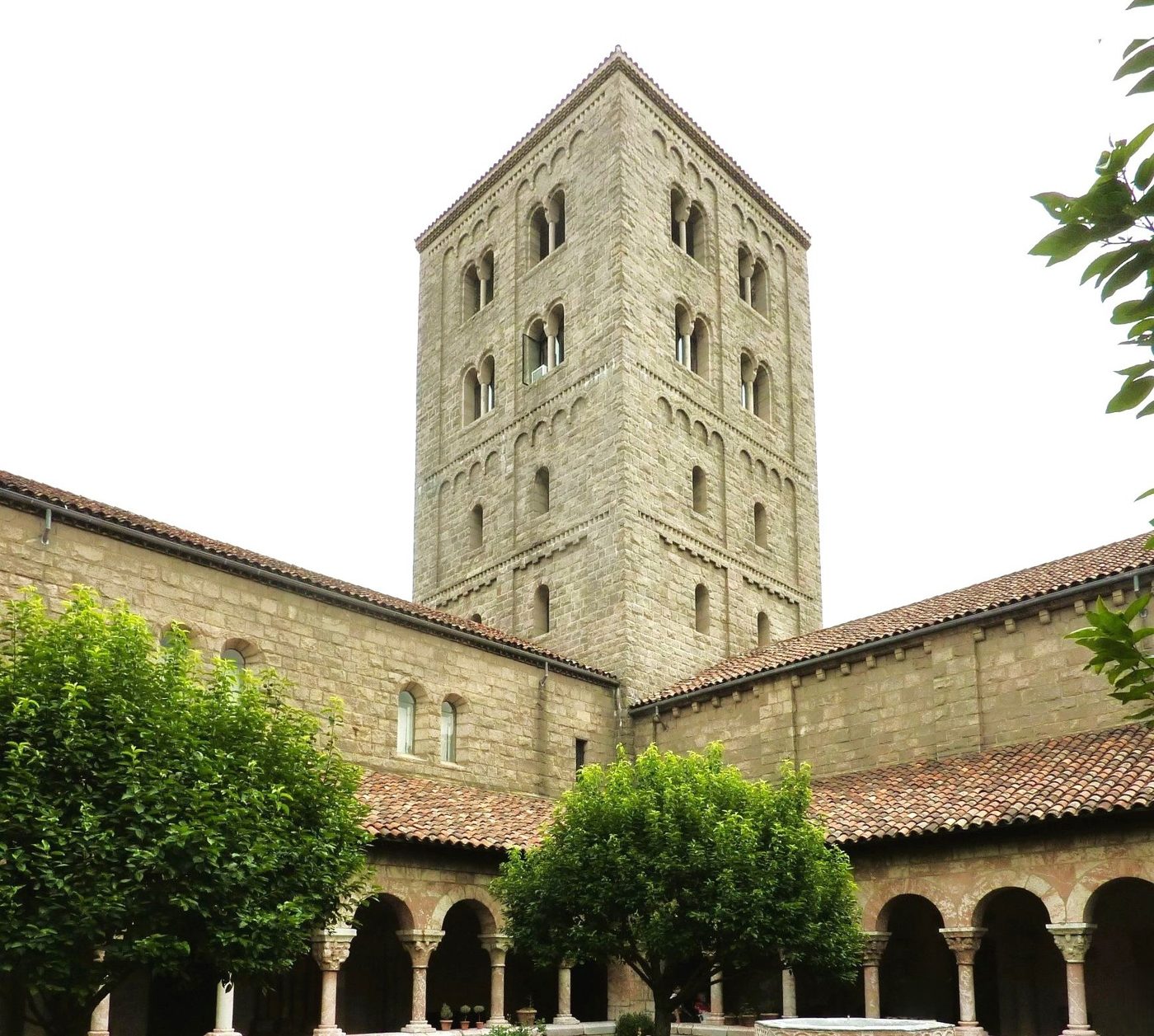 The Cuxa Cloister courtyard with a stone arcade, red tile roofs and the four-story tower behind