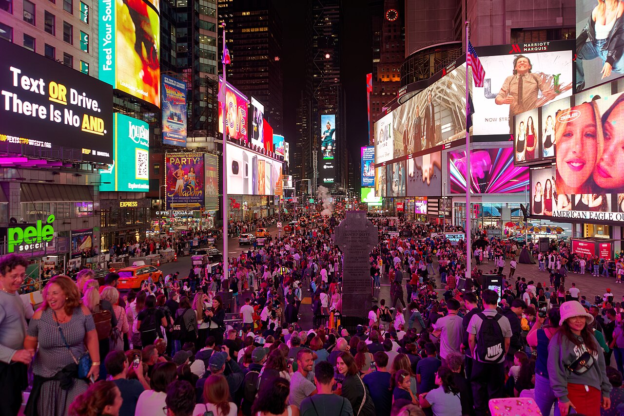 Times Square at night, packed with pedestrians under walls of glowing billboards