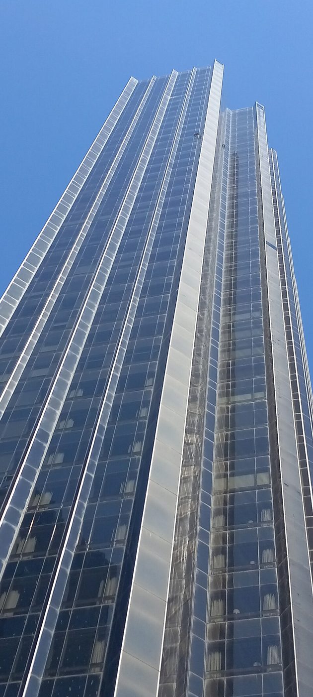 Looking straight up the glass and steel facade of Trump International Hotel and Tower against a blue sky