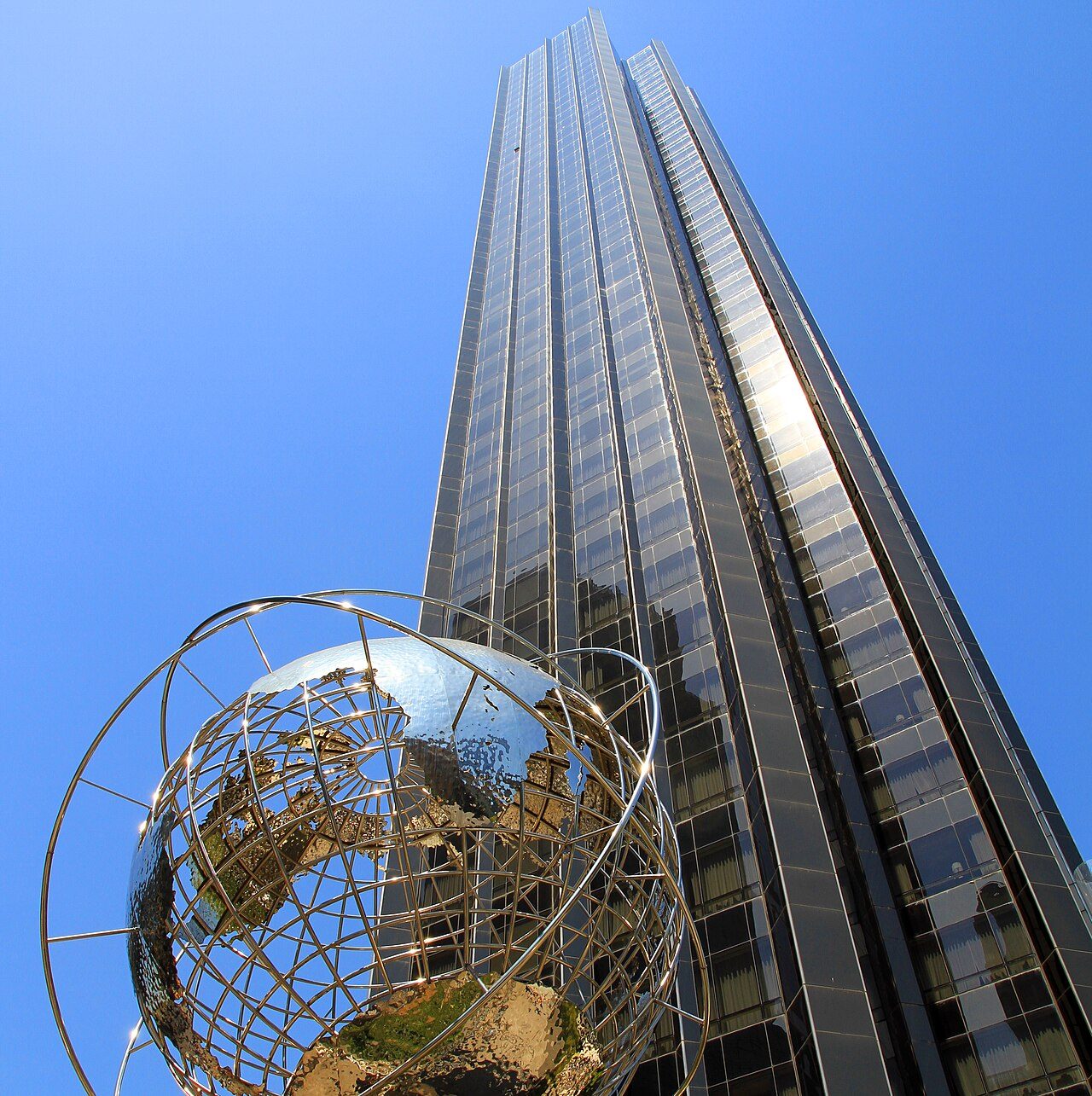 The gold-tinted glass tower of Trump International Hotel and Tower rising behind a stainless-steel globe sculpture at Columbus Circle