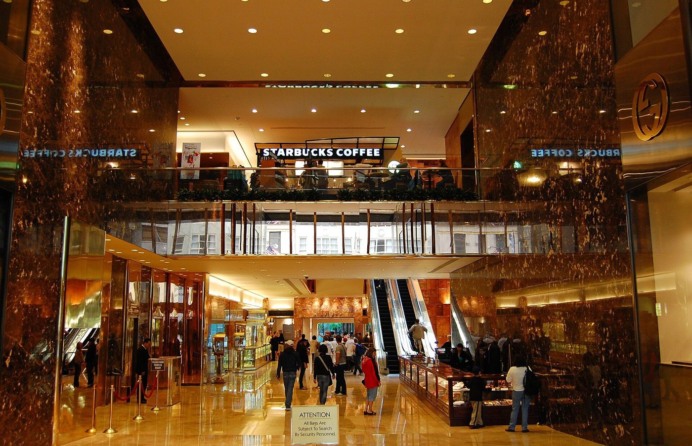 Shoppers on the escalators and balconies of the six-story Trump Tower atrium, lit in gold and pink