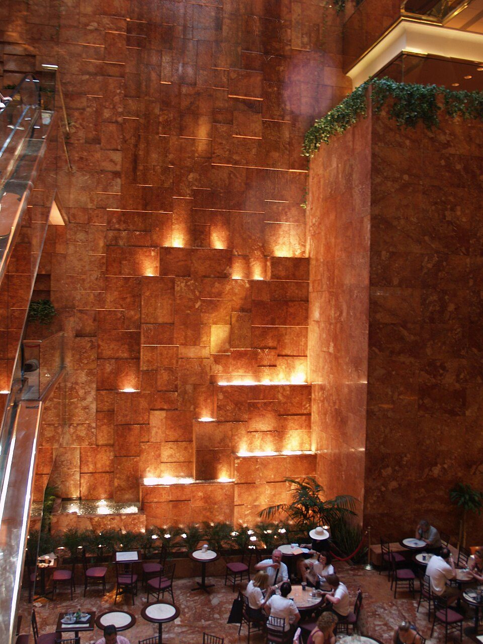 Water falling down a wall of pink and orange marble inside the atrium of Trump Tower, with cafe tables at its base