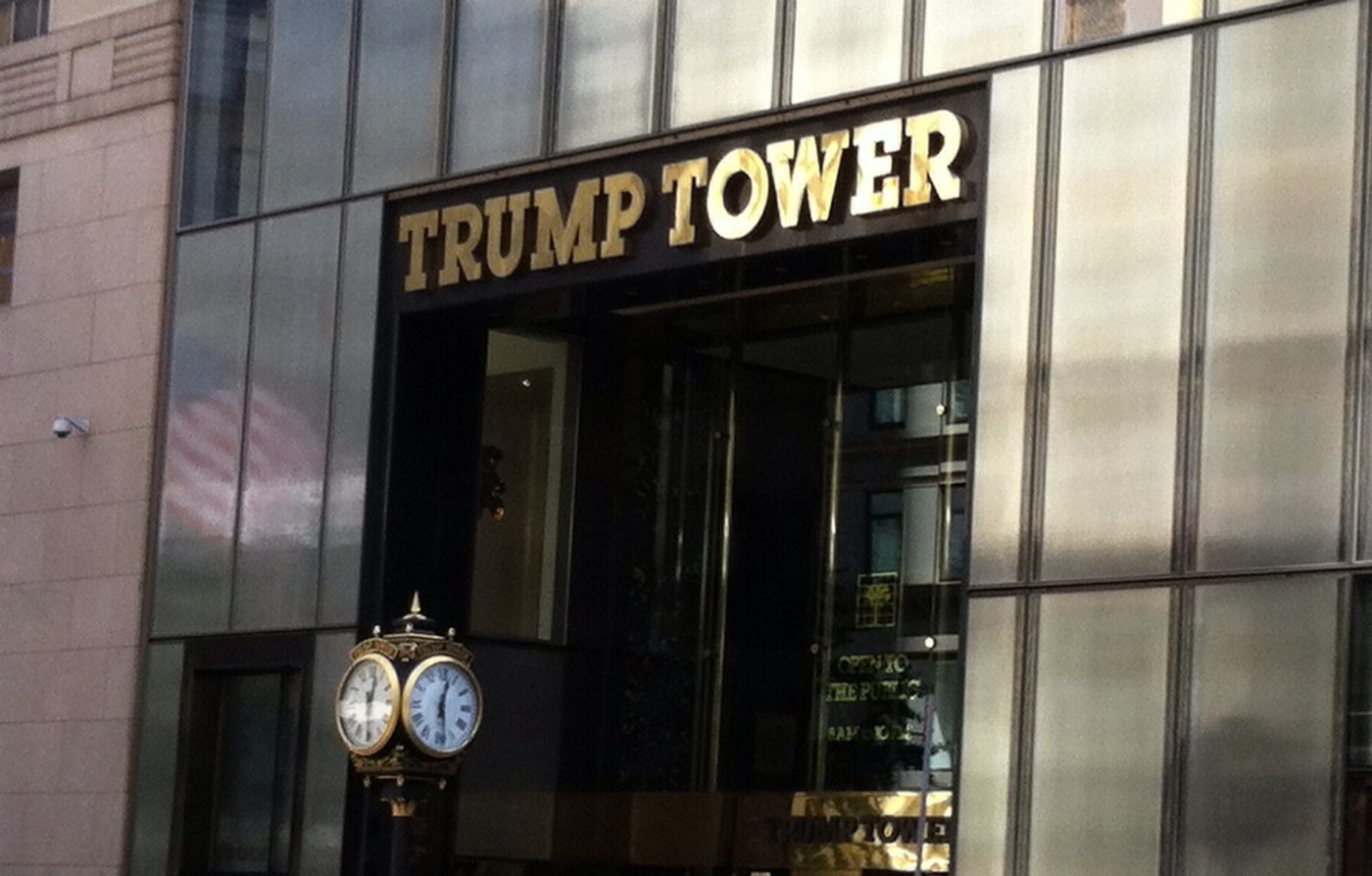 The gold TRUMP TOWER lettering above the glass entrance of 725 Fifth Avenue, with a street clock on the sidewalk