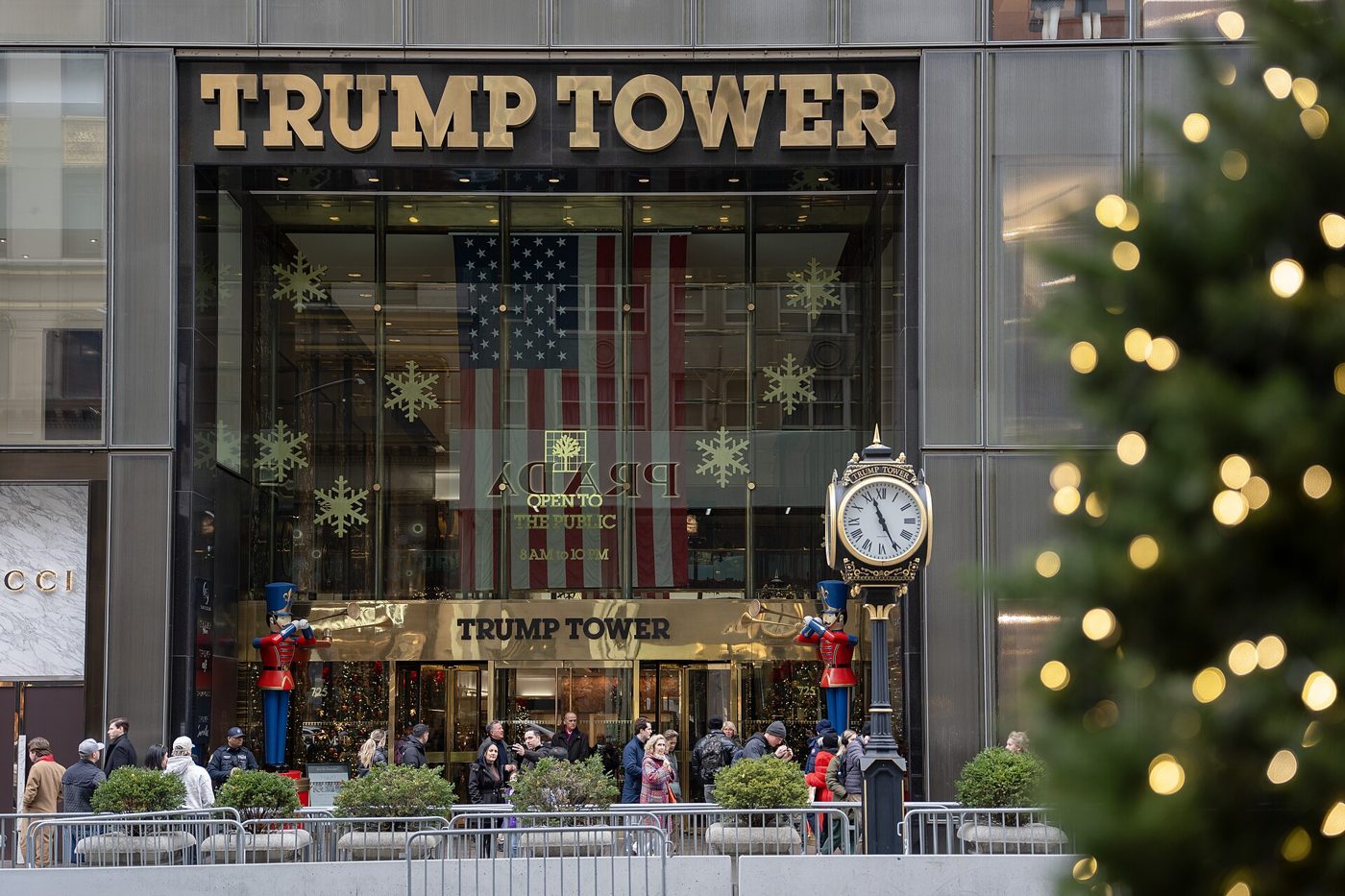 The gold TRUMP TOWER sign over the Fifth Avenue entrance with a decorated Christmas tree and a street clock