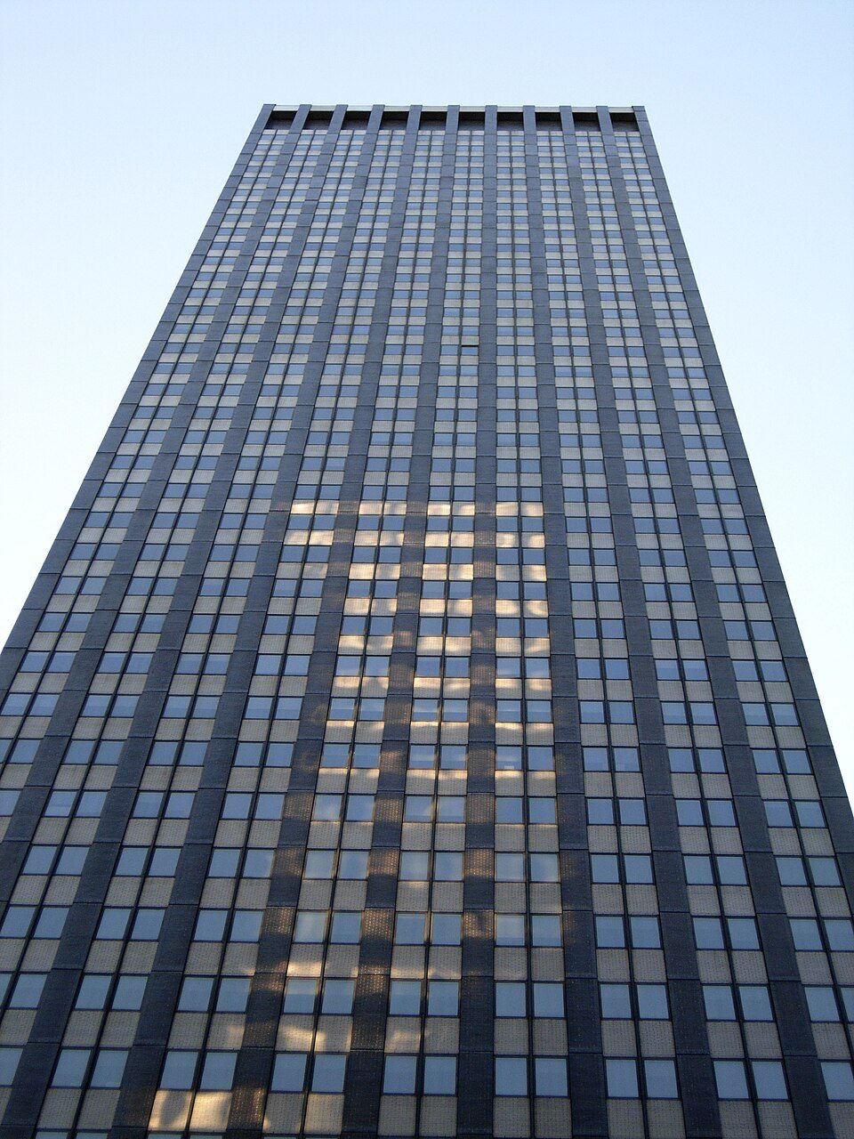 Looking up the bronze-tinted curtain wall of Trump World Tower from its base, with rows of windows narrowing toward the sky