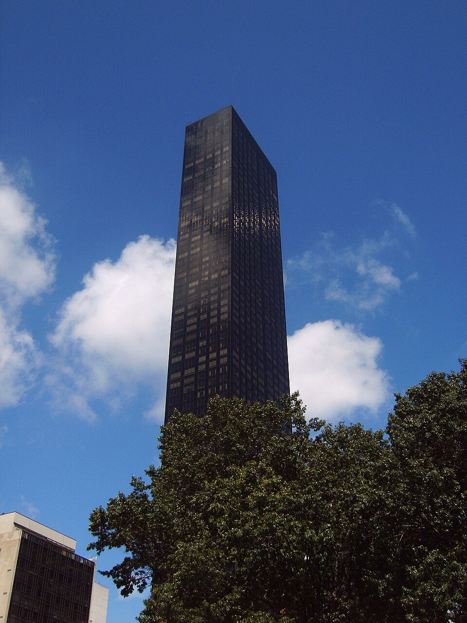 Trump World Tower in dark glass seen between tree branches against a blue sky with white clouds