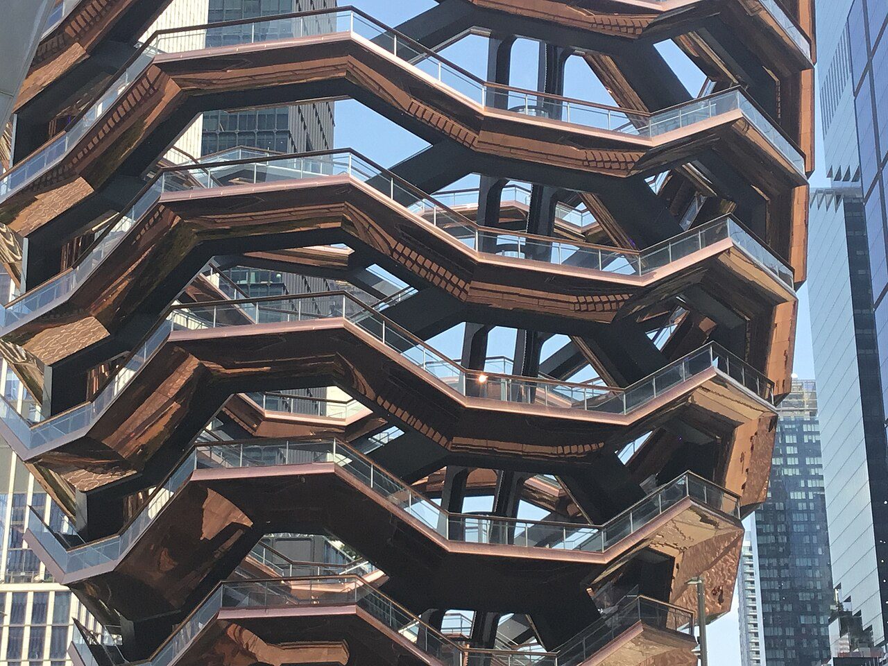 Looking up through the zigzag stairways and landings of the Vessel, with a glass tower behind