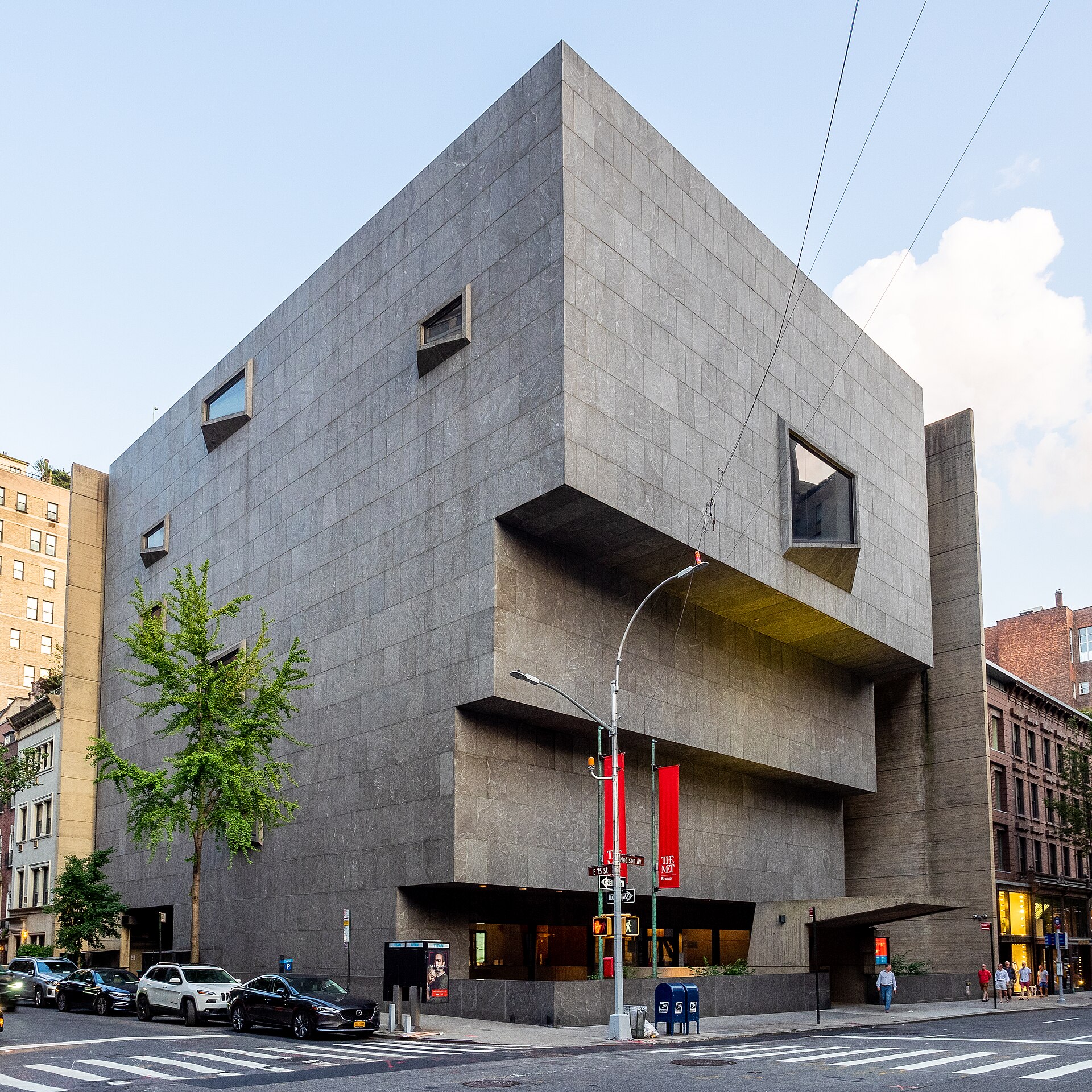 The former Whitney Museum at 945 Madison Avenue, a heavy granite building that steps outward as it rises, with a trapezoid window on the upper facade