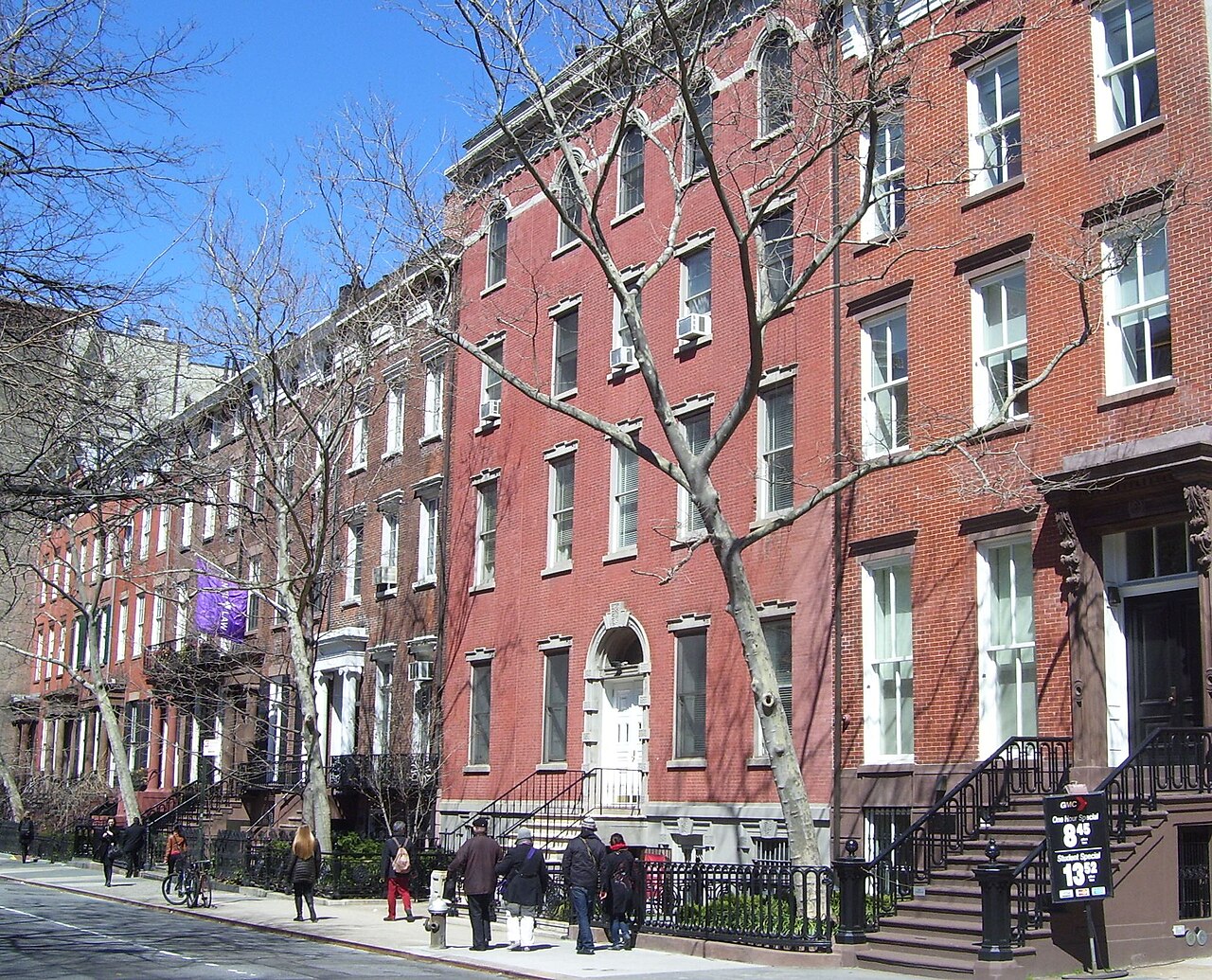A row of red brick Greek Revival townhouses with white doorways on the north side of Washington Square