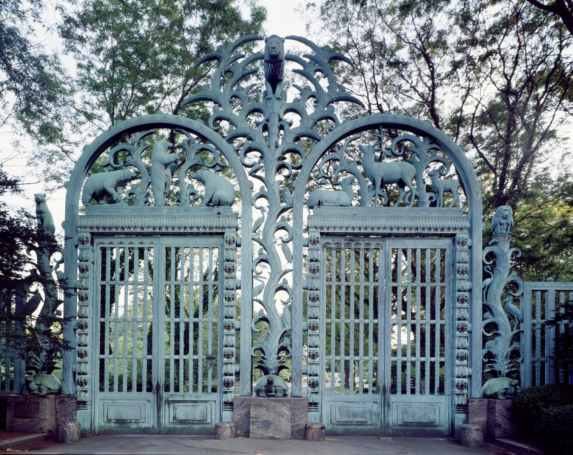 The Rainey Memorial Gates, tall greenish bronze gates covered with sculpted animals and plants, closed between granite lodges